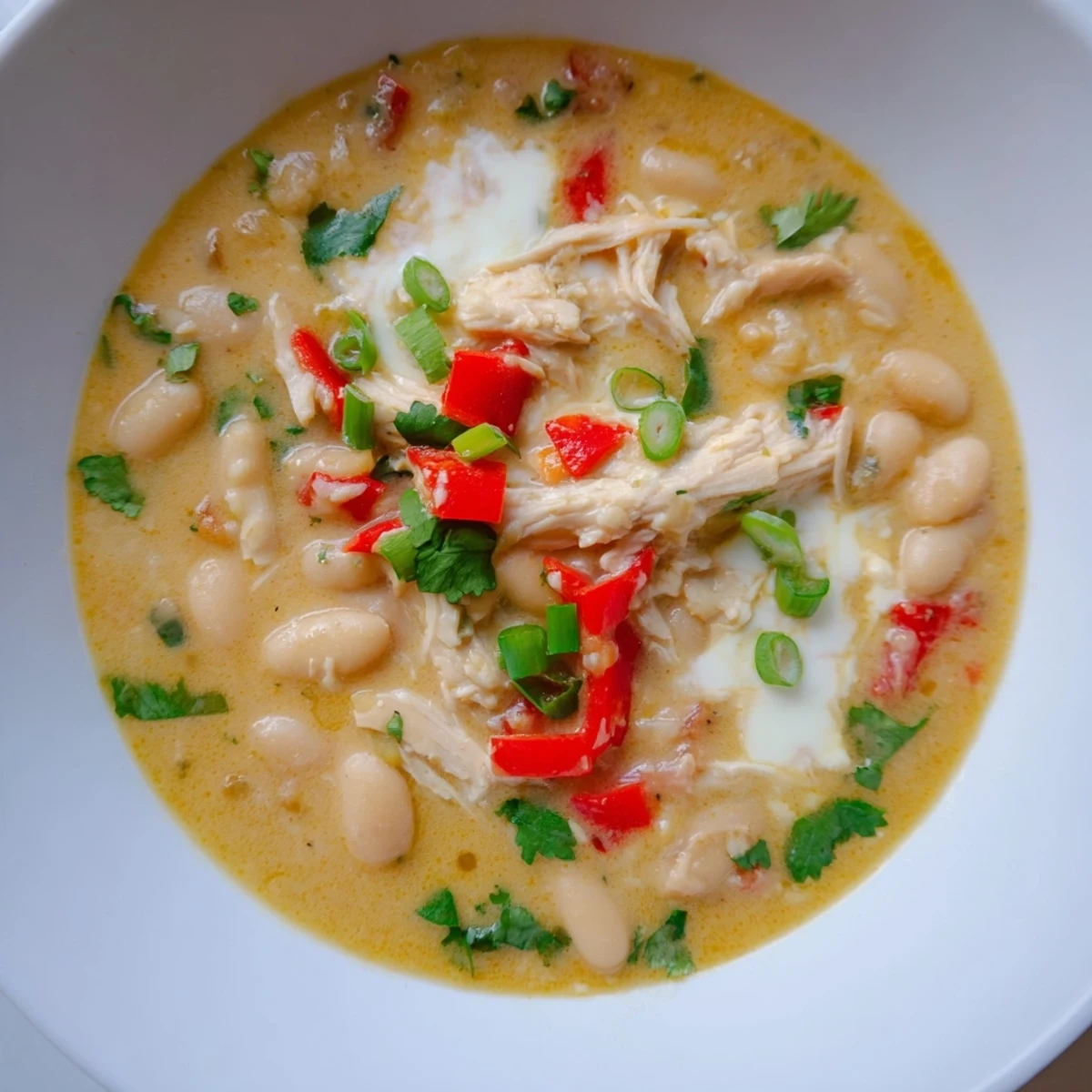 A steaming bowl of Creamy White Chicken Chili with beans, garnished with fresh cilantro and cheese.