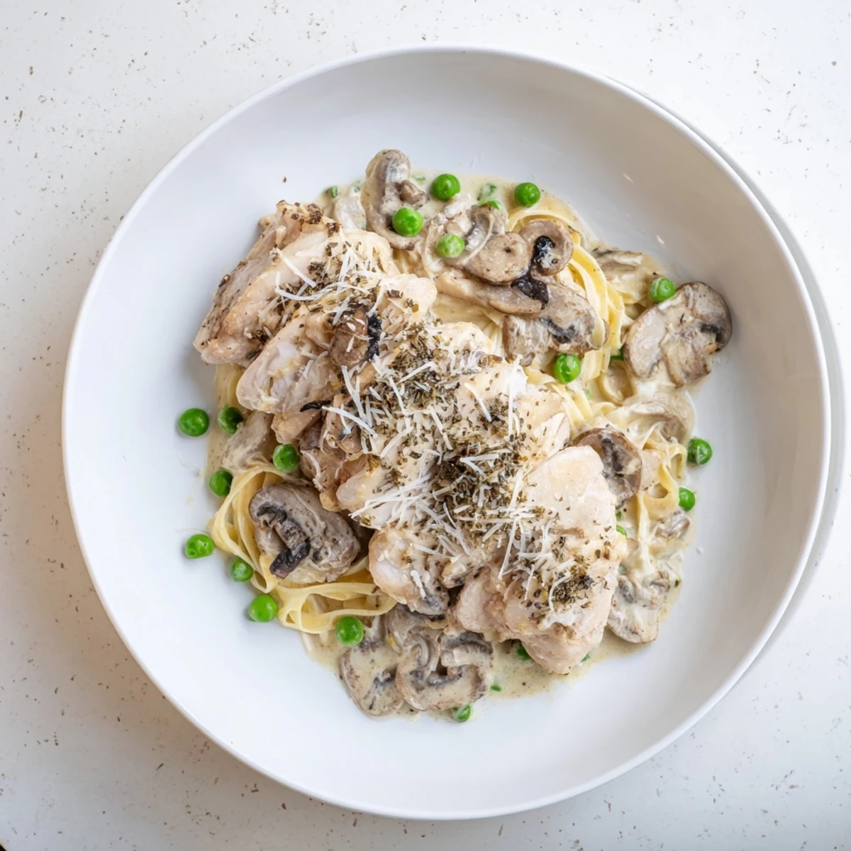 A close-up of creamy, flavorful Creamy Chicken Alfredo, garnished with Parmesan and fresh herbs over pasta.