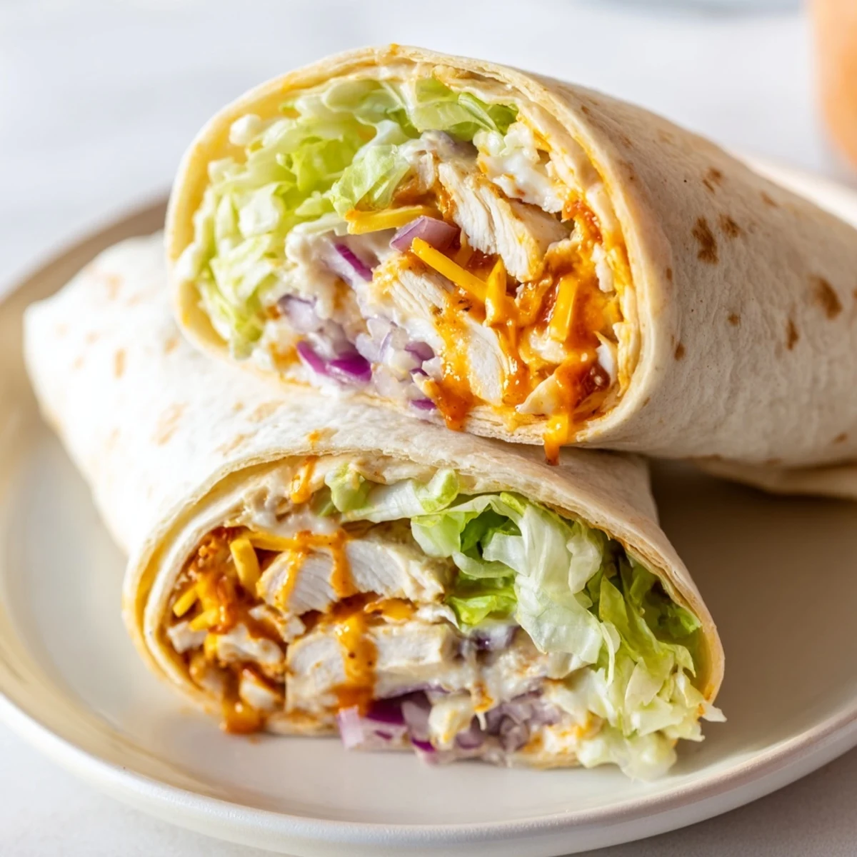 A close-up of a Buffalo Ranch Chicken Wrap, sliced in half to reveal juicy buffalo chicken, shredded cheddar, and crisp romaine inside a golden-brown tortilla.