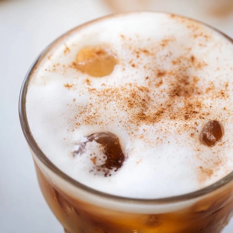 Iced Chai Tea with Cold Foam in a tall glass, layered over ice cubes and topped with a thick, creamy foam and a light dusting of cinnamon.