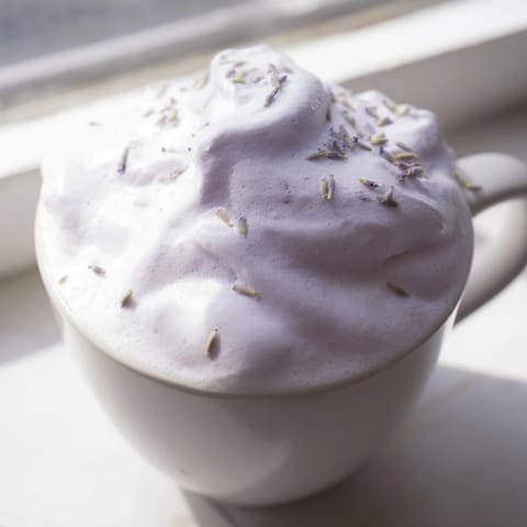 Creamy espresso and lavender syrup topped with fluffy whipped foam in a glass mug, perfect for a relaxing afternoon treat.  