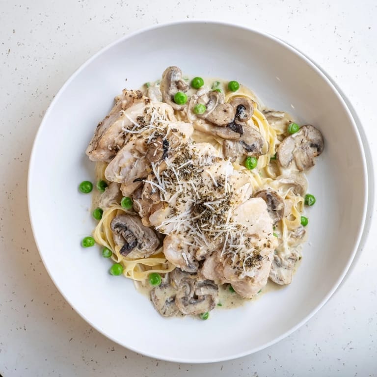 A close-up of creamy, flavorful Creamy Chicken Alfredo, garnished with Parmesan and fresh herbs over pasta.