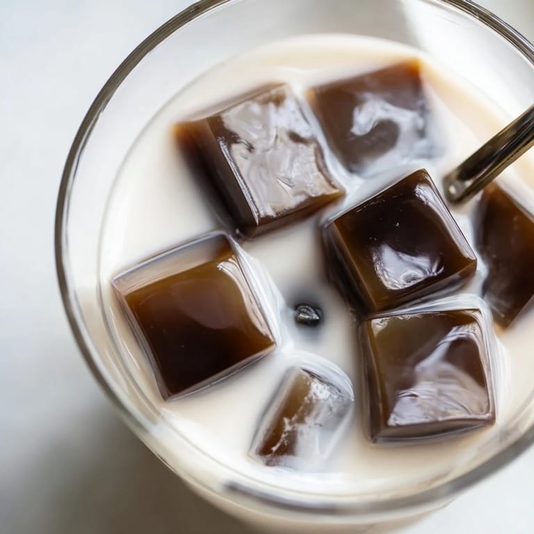 Sweet, bouncy coffee jelly cubes piled high in a glass with ice and creamy milk.  